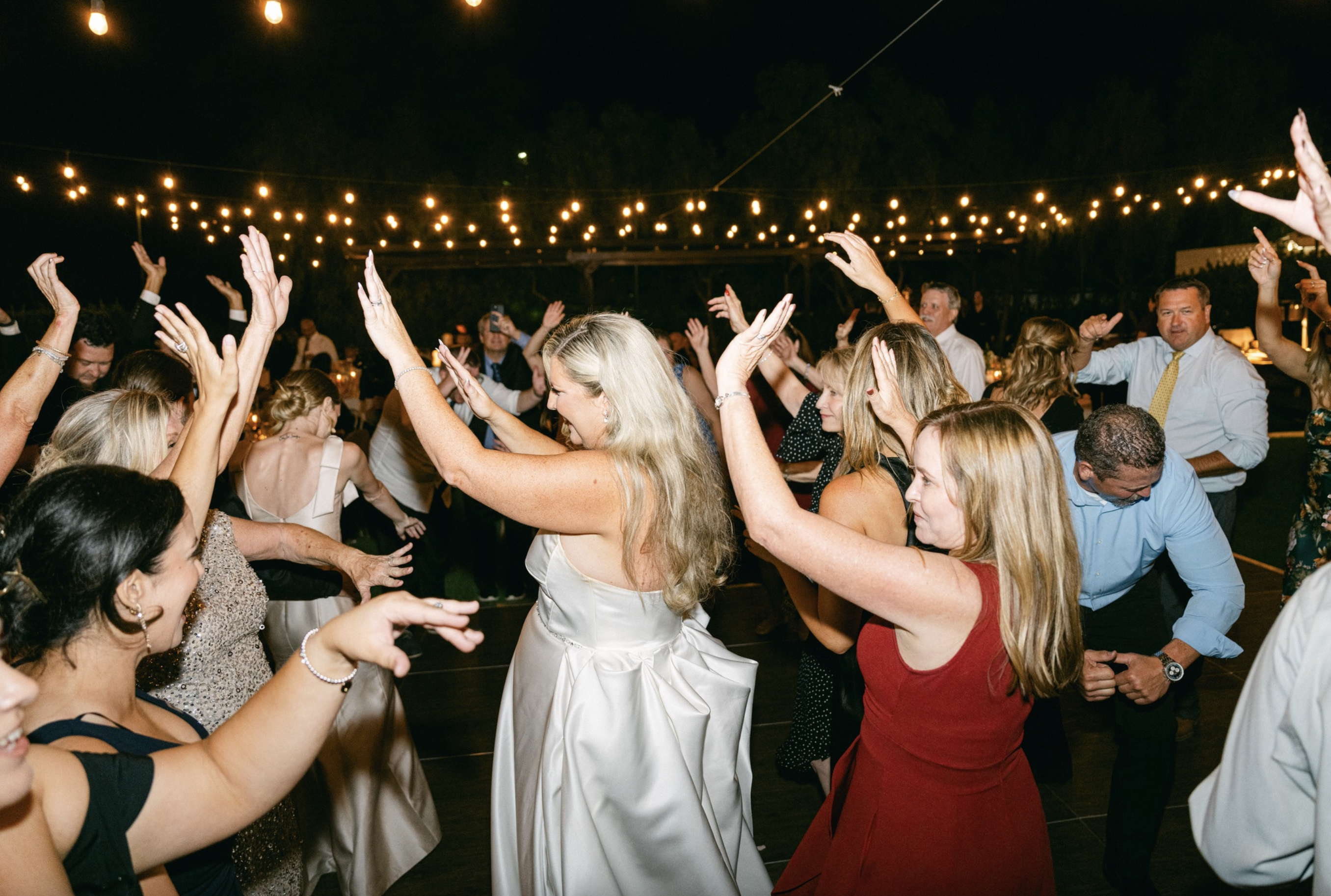 People dancing joyfully at a nighttime event under string lights.