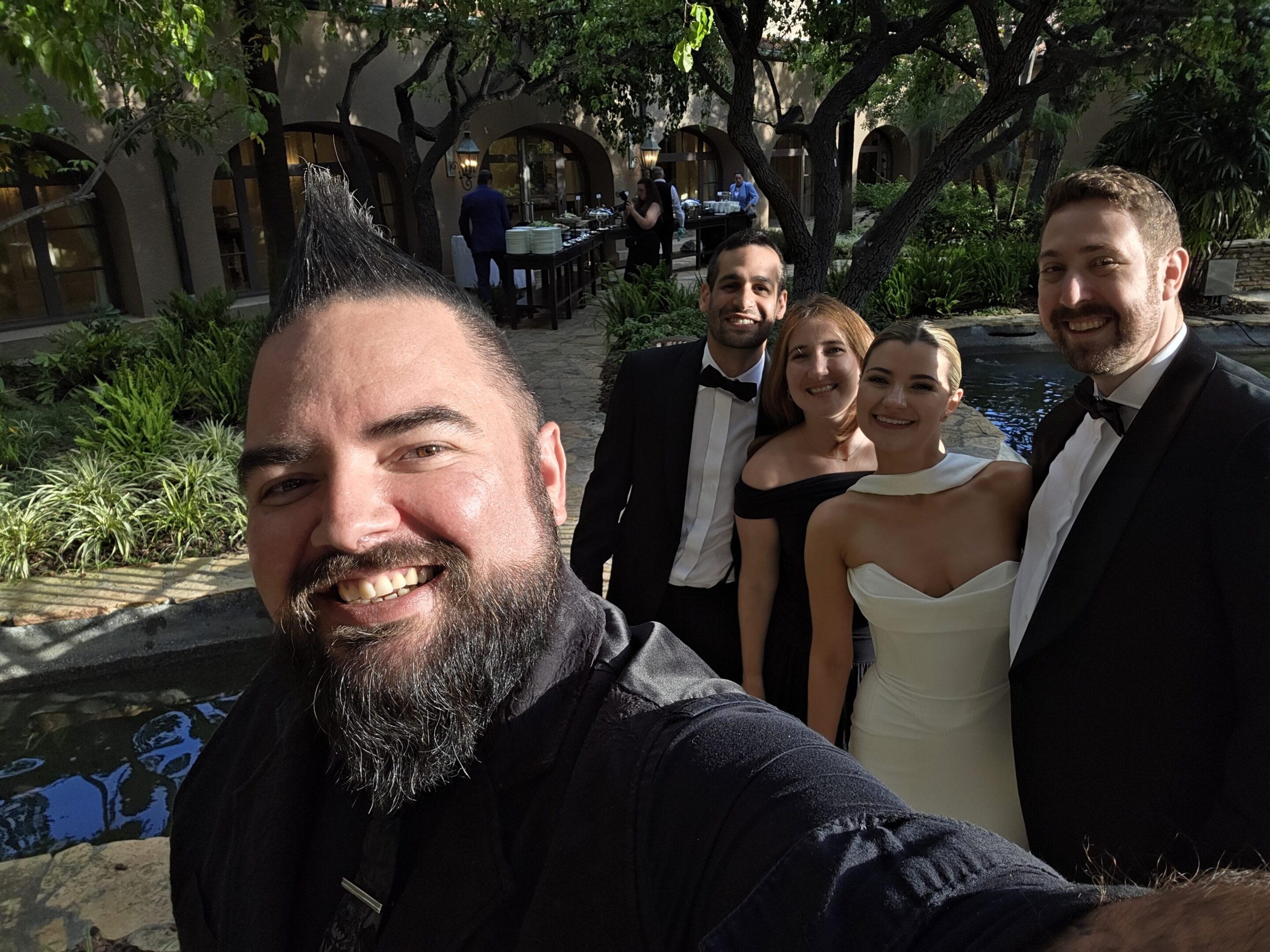 A group selfie with four people dressed formally, smiling outdoors.