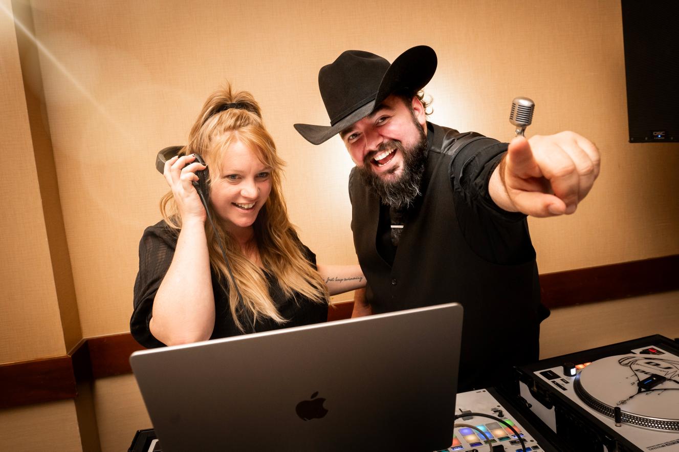 Two DJs smiling and working together at a laptop with DJ equipment.