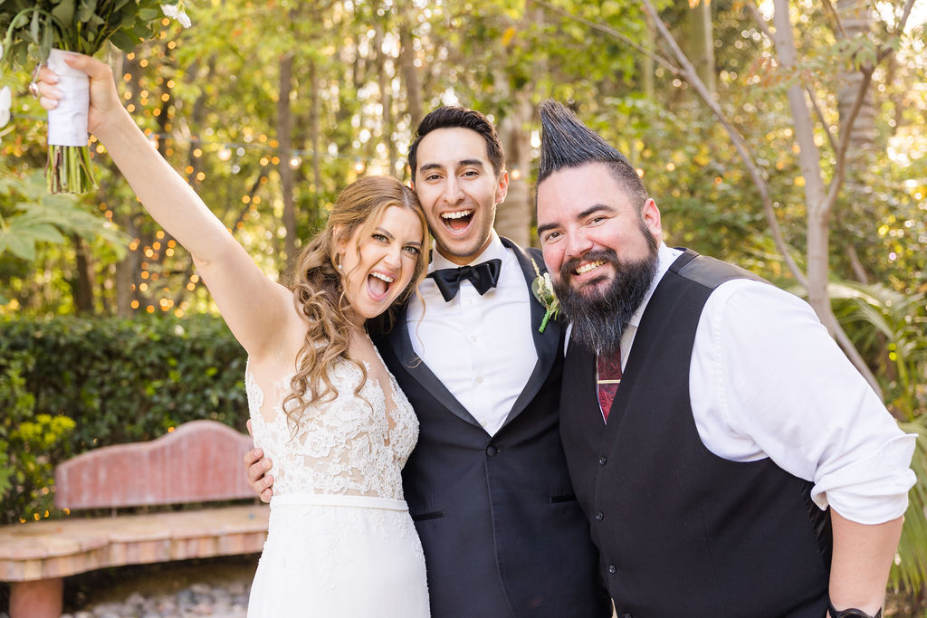 Joyful bride, groom, and bearded man posing outdoors at a wedding.