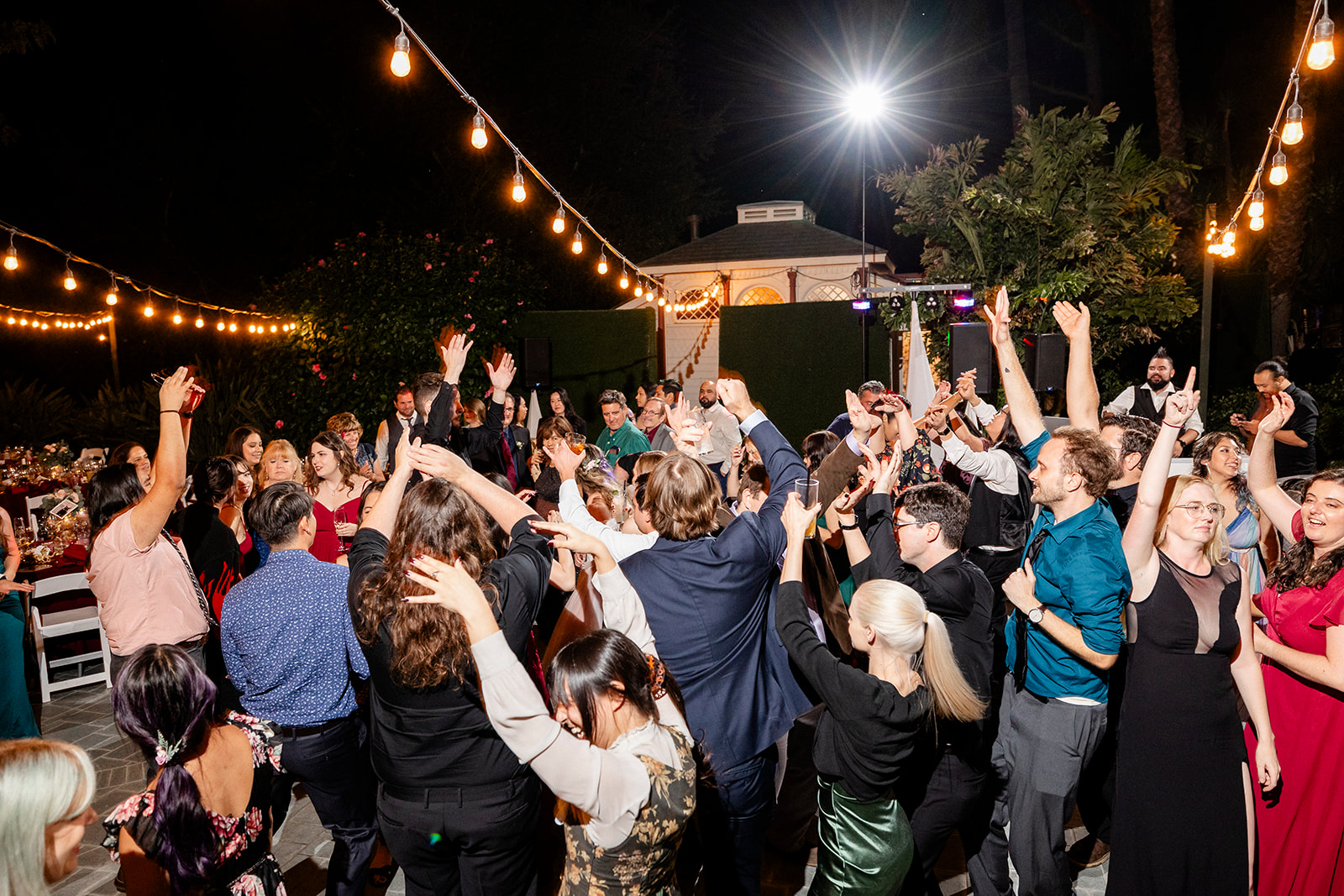 A lively outdoor party with people dancing under string lights.