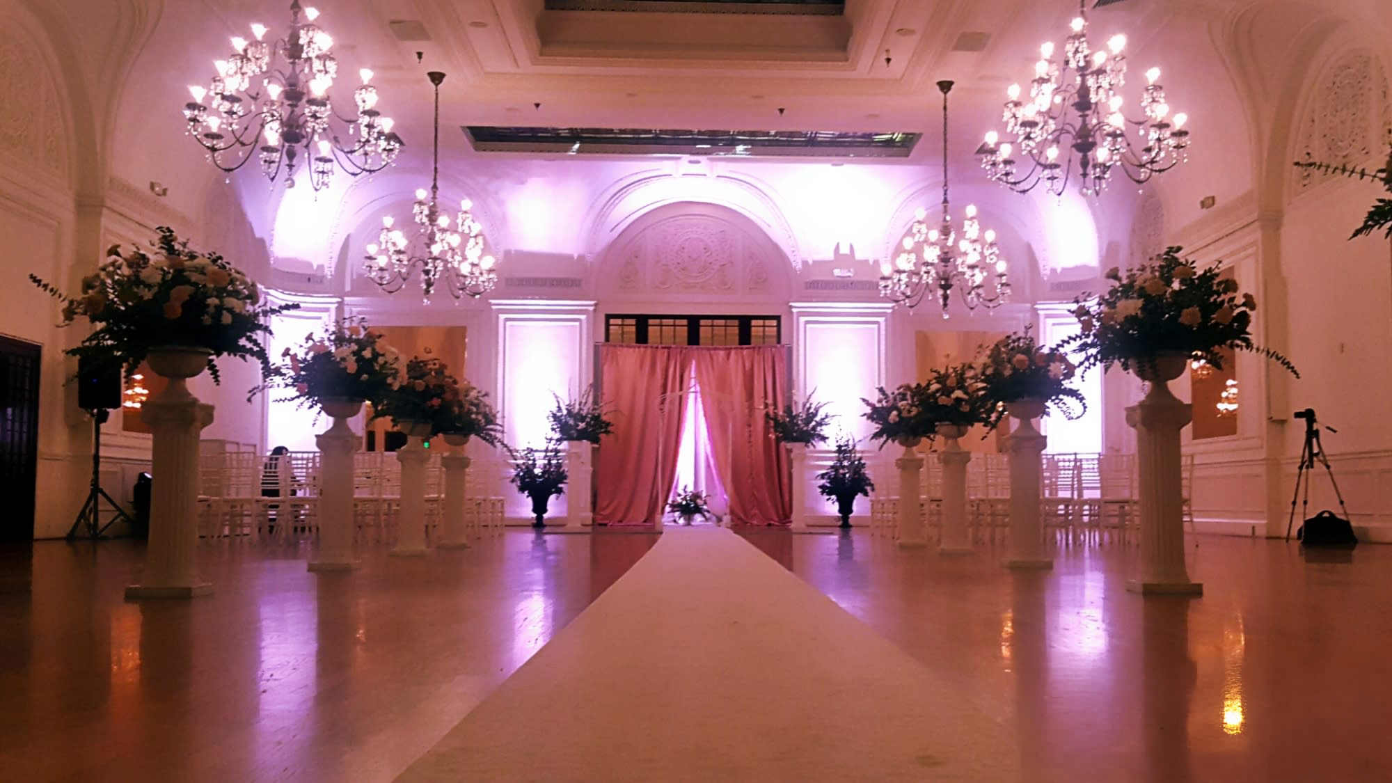 Elegant wedding aisle with soft pink lighting and floral decorations.
