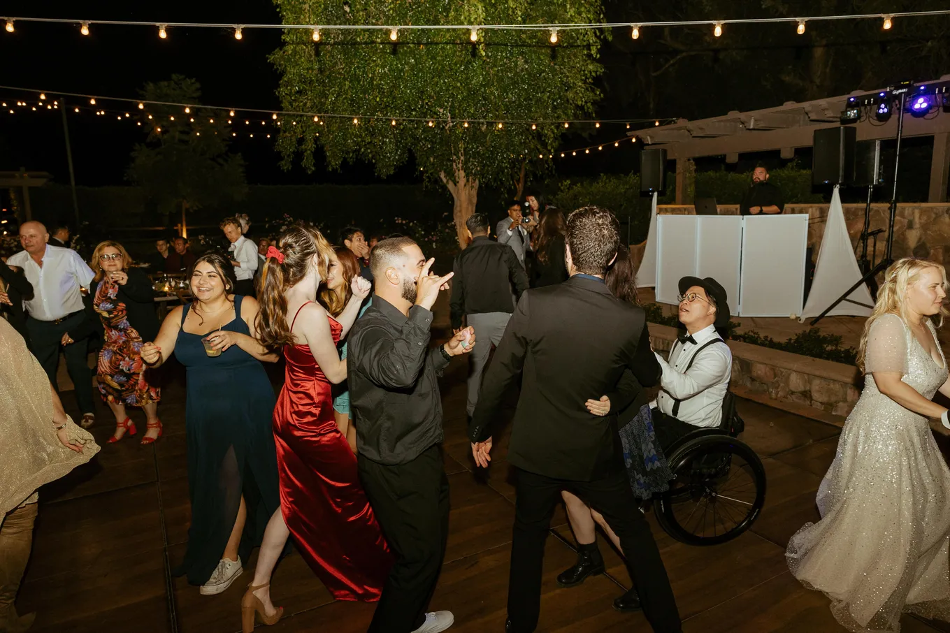People dancing joyfully under string lights at a nighttime outdoor event.