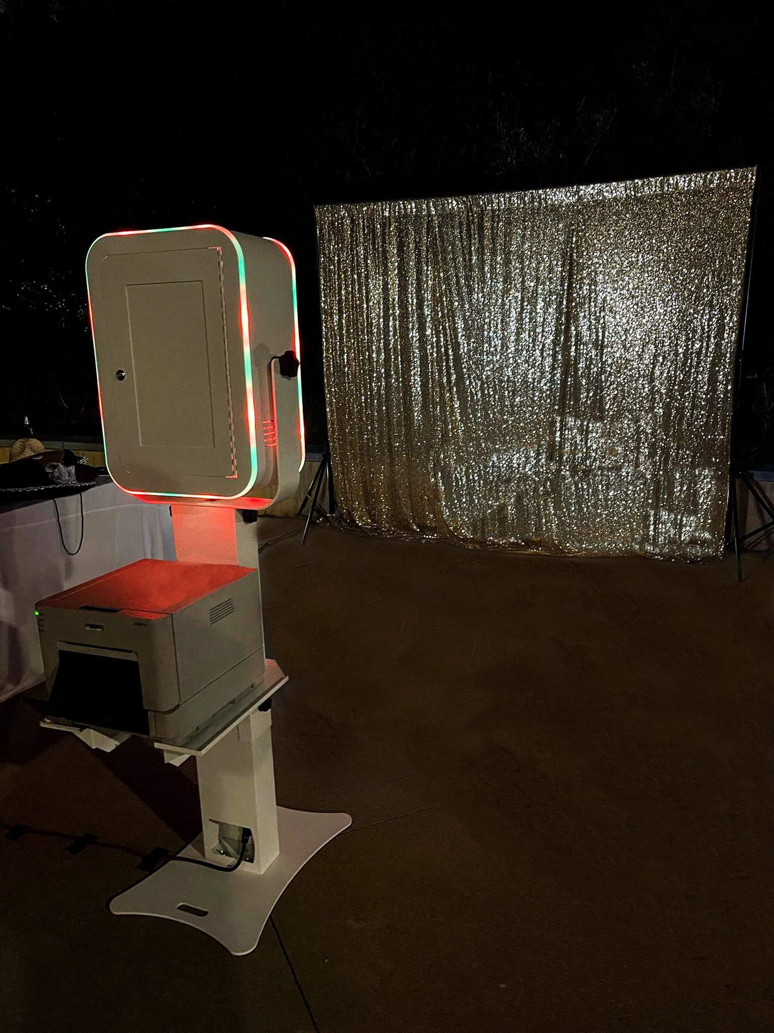 Photo booth setup with a shimmering silver backdrop and illuminated camera.